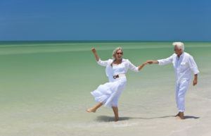 Happy Senior Couple Dancing Holding Hands On A Tropical Beach